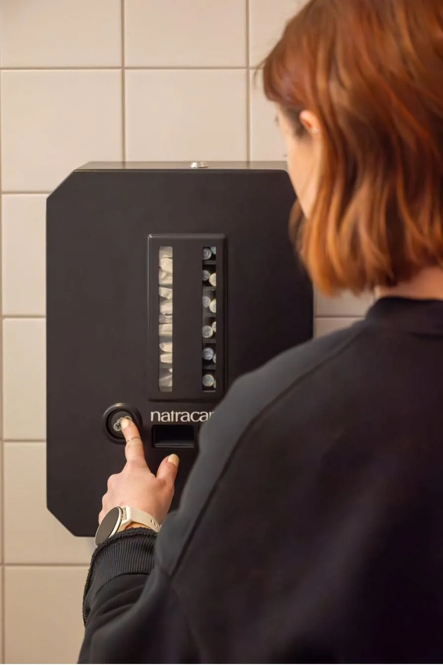 Person trycker på knappen för att ta ett mensskydd ur Kvins dispenser