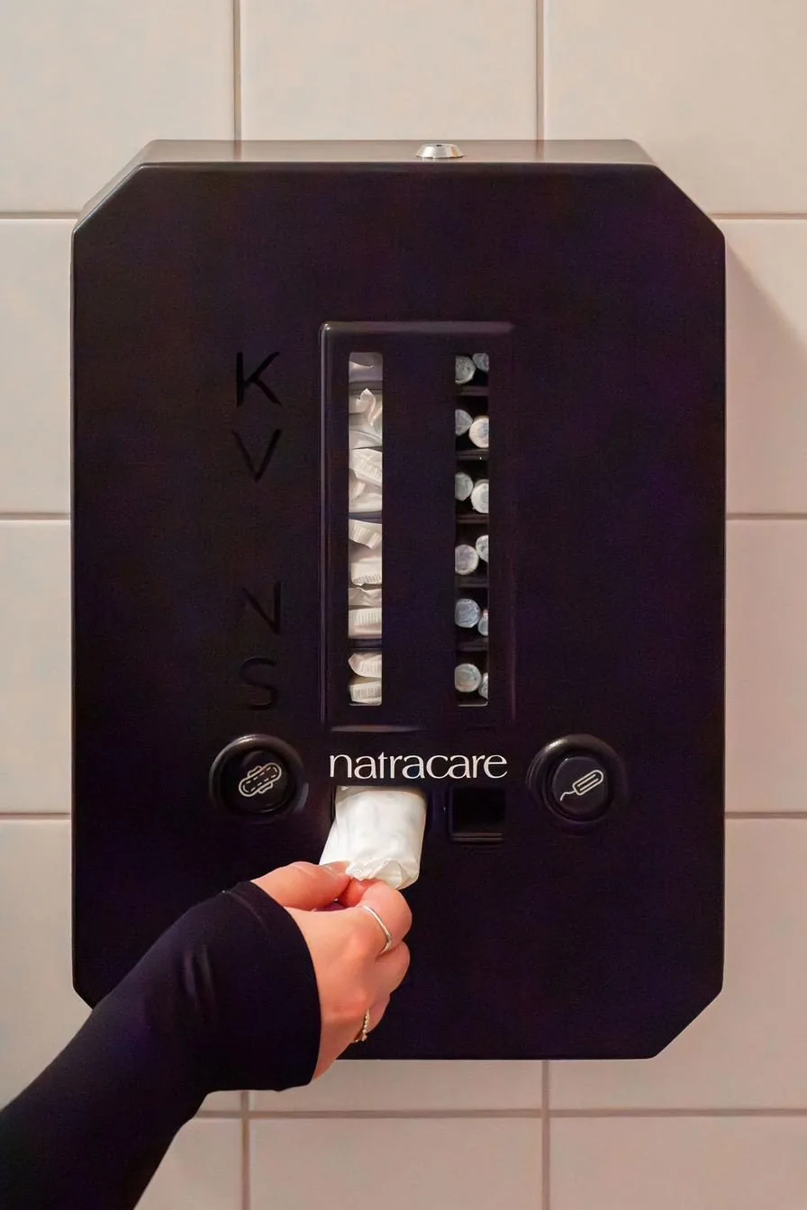 Hand tar en binda ur Kvins mensskyddsdispenser på en kaklad toalettvägg