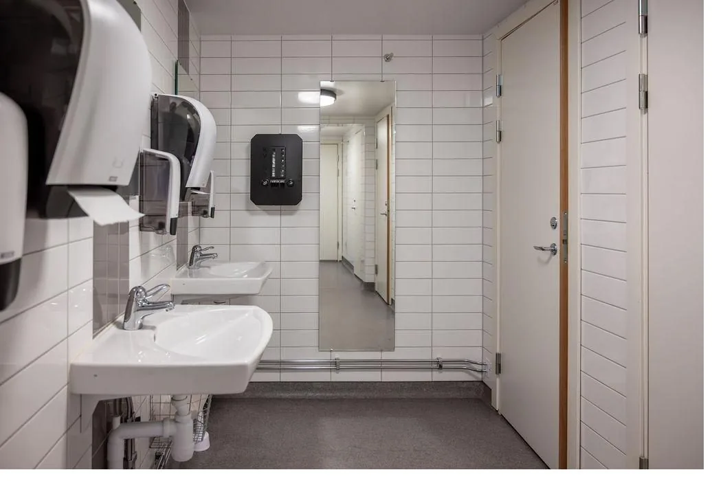 Toalettutrymme på arbetsplats med Kvins mensskyddsdispenser på väggen